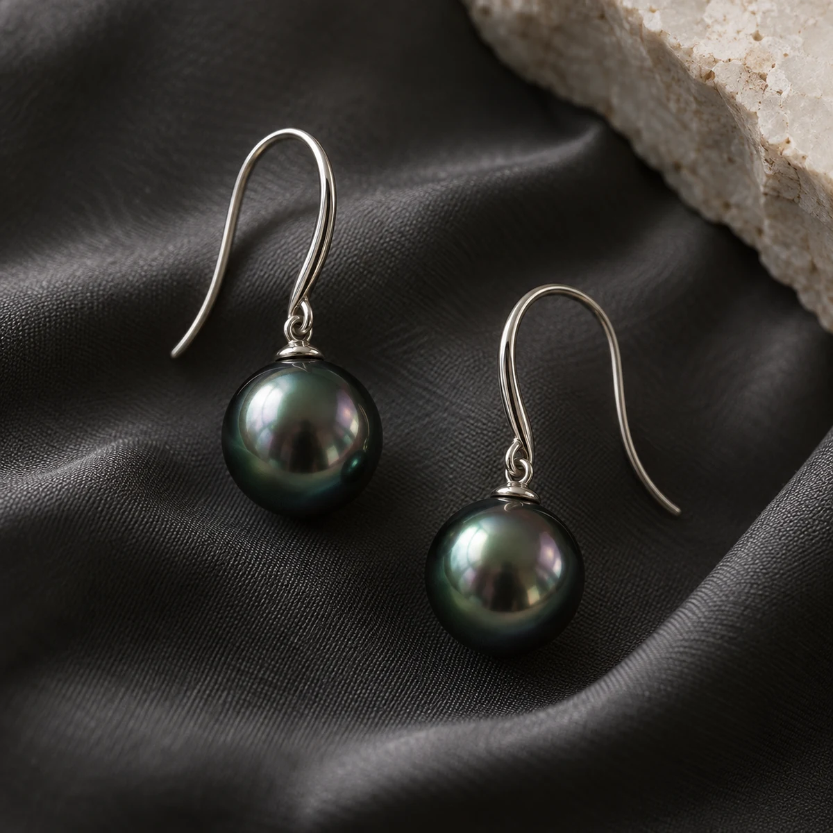 Pair of dark Tahitian-style pearl drop earrings on charcoal silk; concept photograph