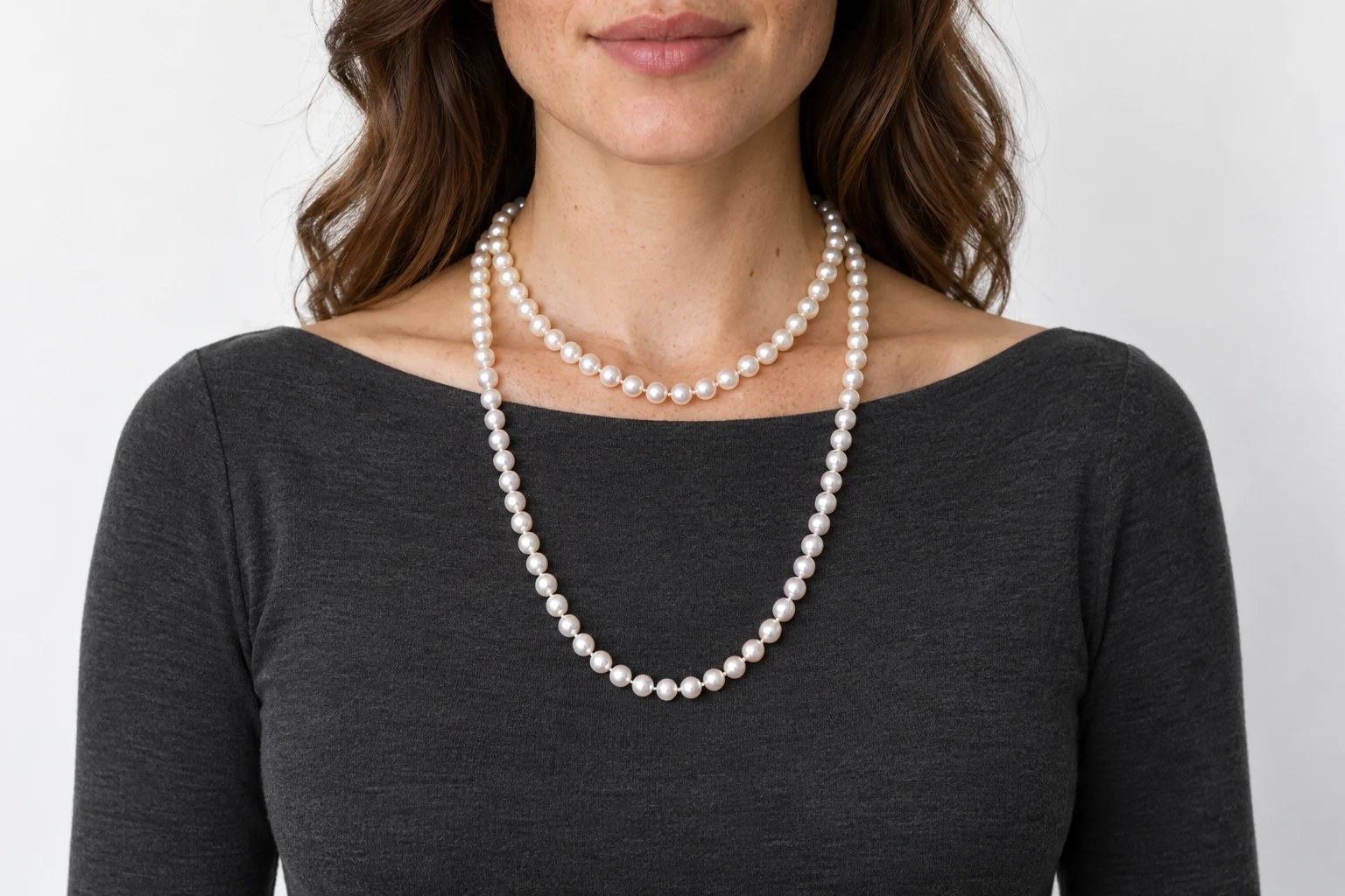 A shorter pearl strand at the collarbone and a longer strand over a charcoal neckline