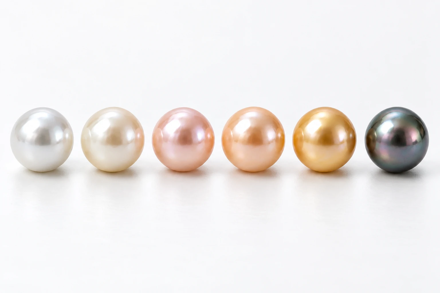 Six high-luster pearls progressing from white and cream to blush, peach, golden and dark peacock colors