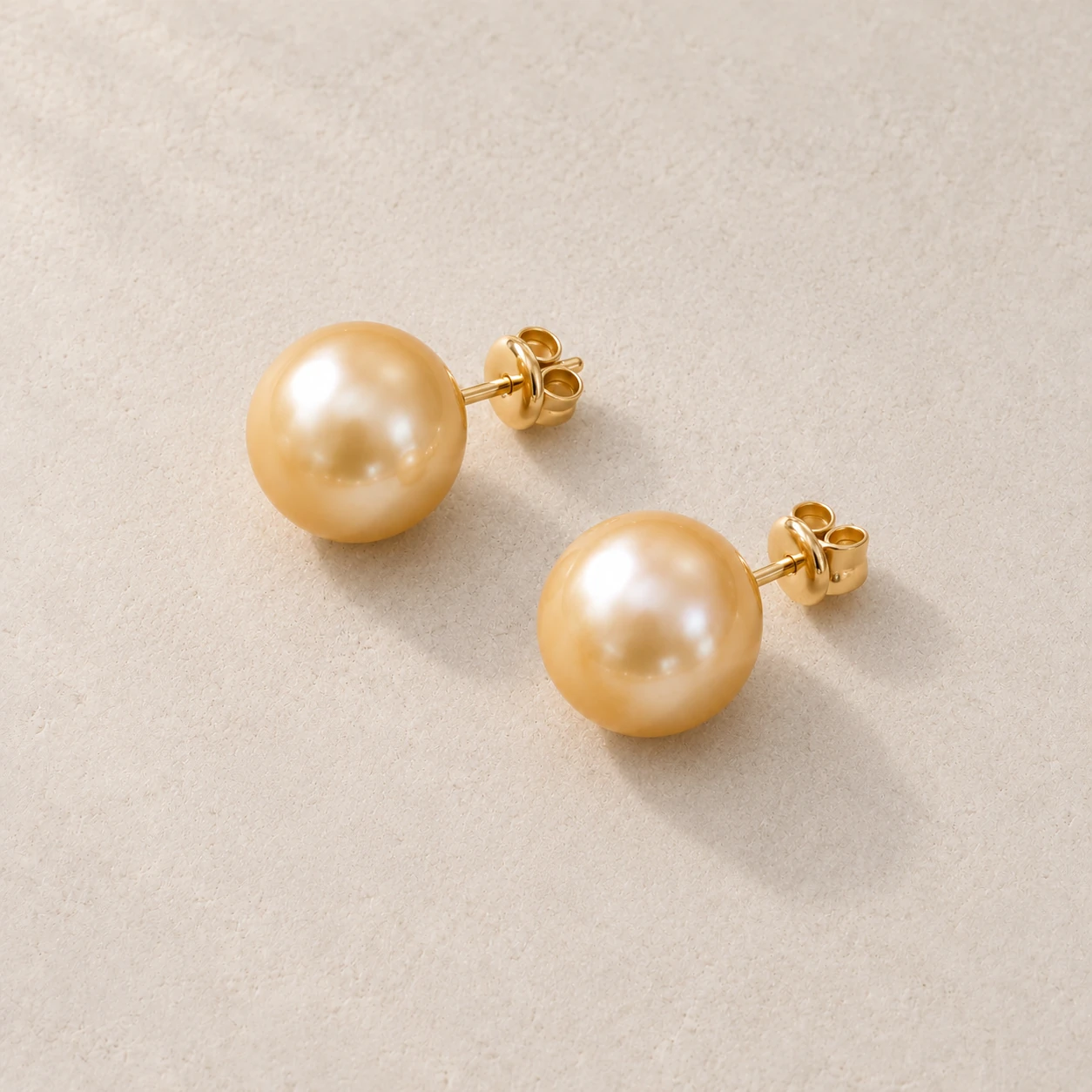 Pair of golden South Sea-style pearl stud earrings on pale warm-grey stone; concept photograph